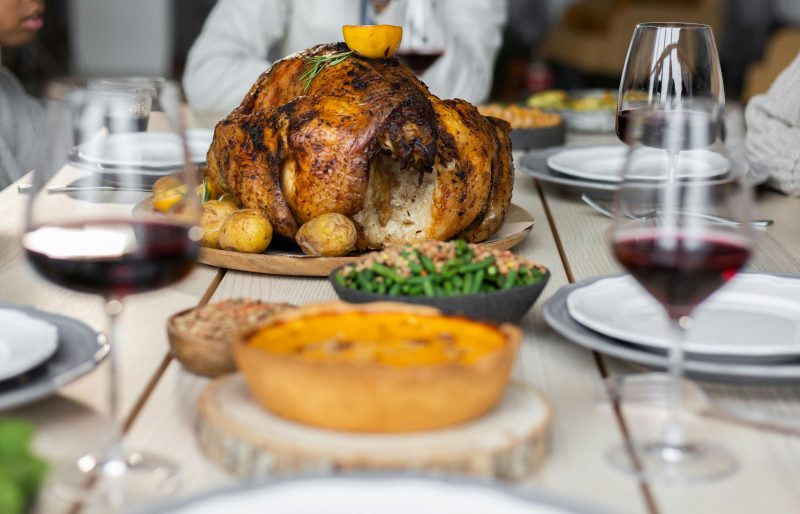Thanksgiving table featuring a cooked turkey and glasses of red wine.