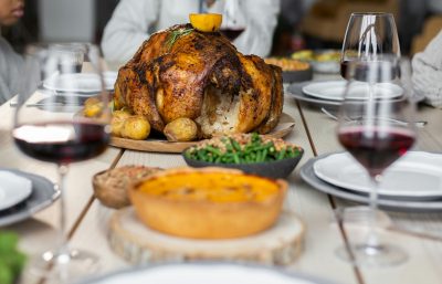 Thanksgiving table featuring a cooked turkey and glasses of red wine.