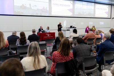 A crowd of people watching a panel discussion of five presenters